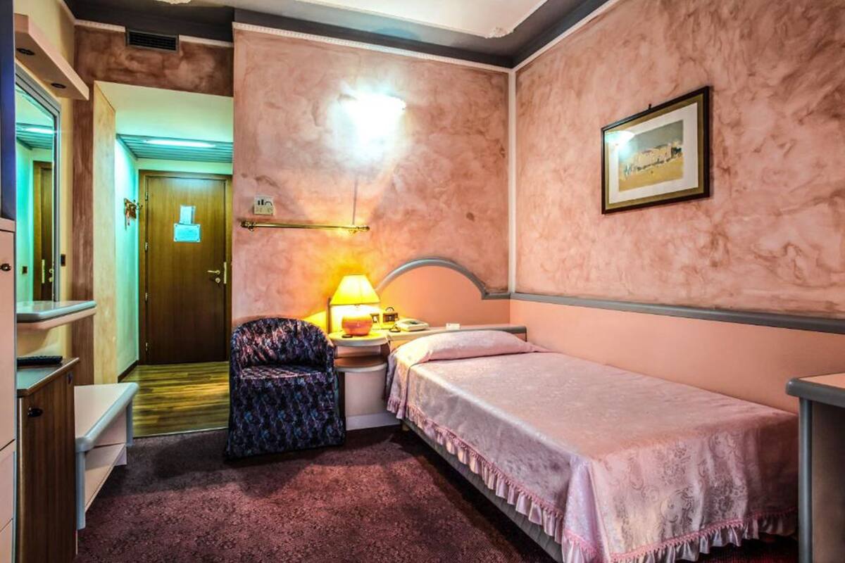 A hotel room with a single bed, a chair, a desk, and a lamp.