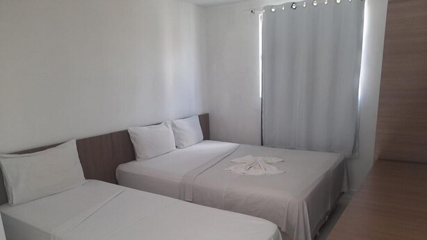 Une chambre d’hôtel avec deux lits simples, une tête de lit en bois, une petite table et un rideau.
