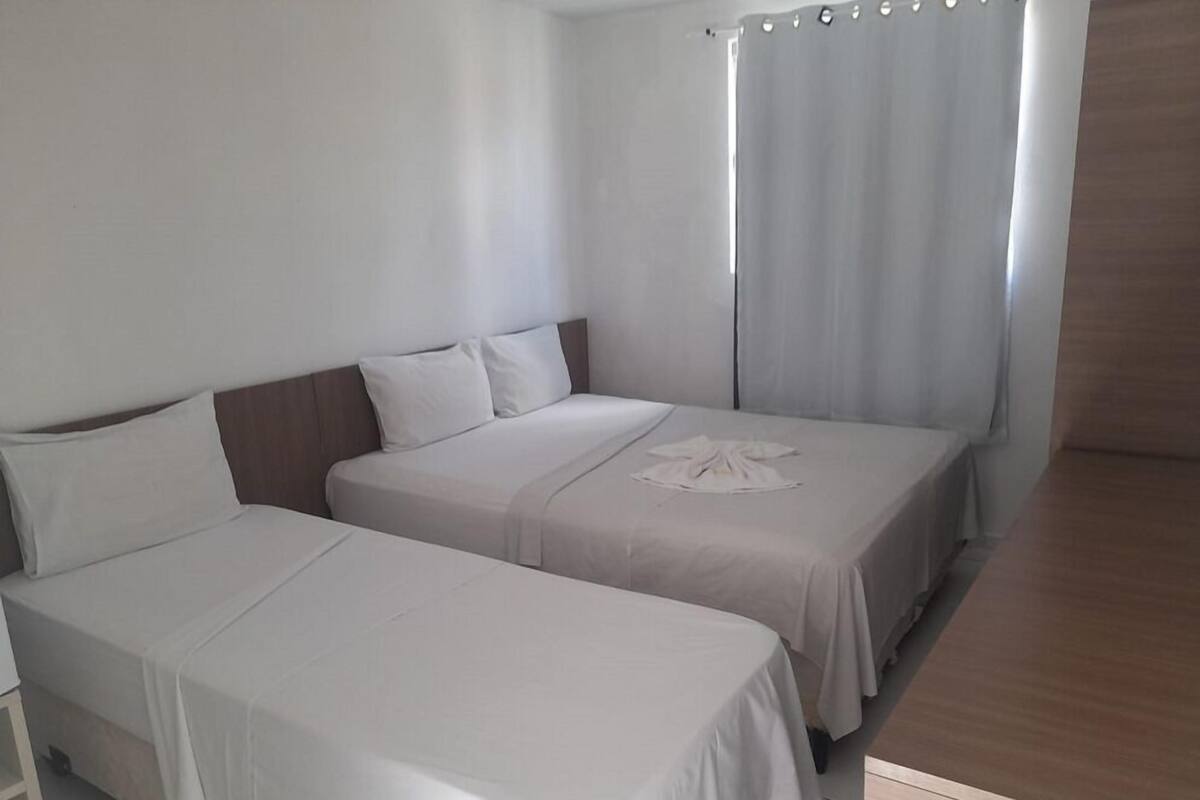 Ett hotellrum med två separata sängar, en sänggavel i trä, ett litet bord och en gardin.