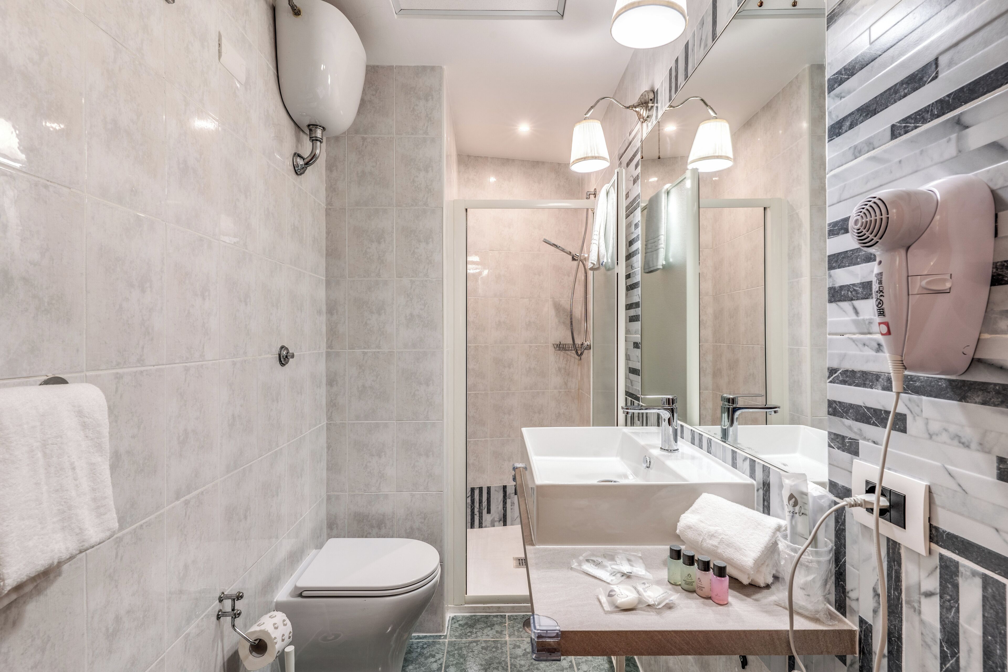 A modern bathroom with a toilet, bidet, and shower area. There is a vanity with a mirror, sink, and towel rack.