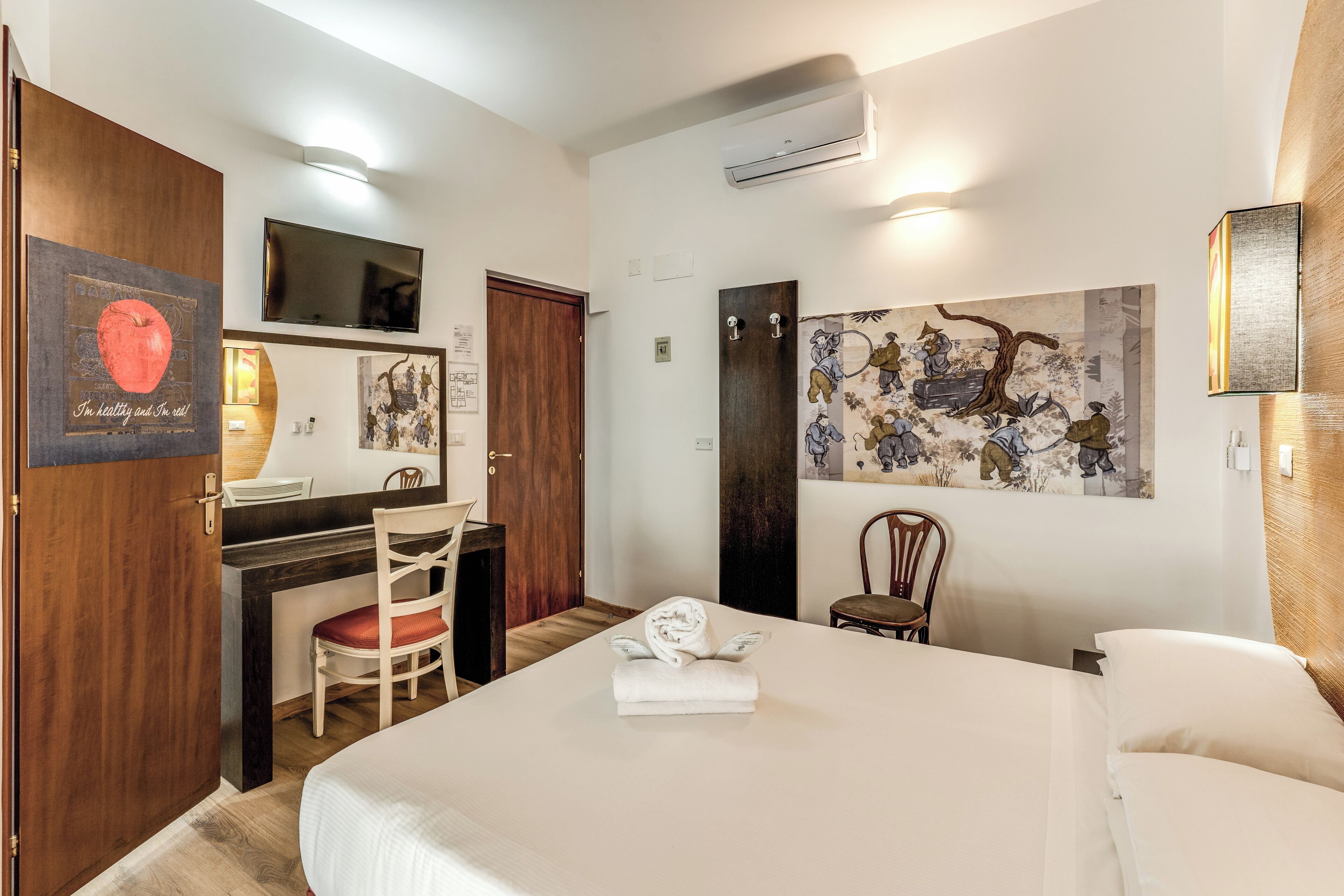 A hotel room with a bed, desk, chair, and artwork on the walls.
