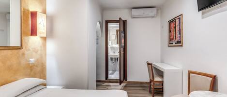 A hotel room with a bed, a desk, a chair, and a TV.