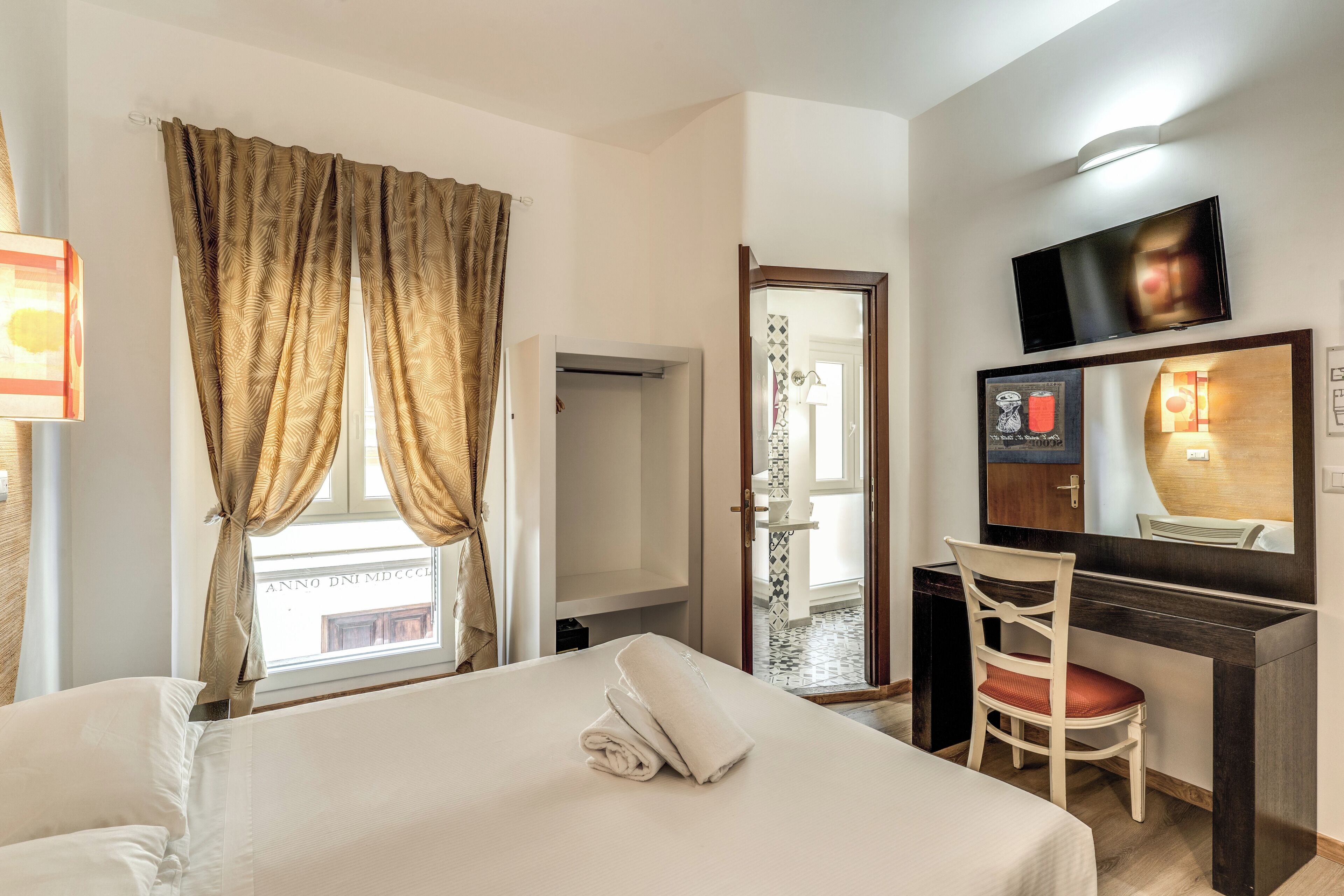 A hotel room with a bed, a desk, a chair, a TV, and a window with curtains.