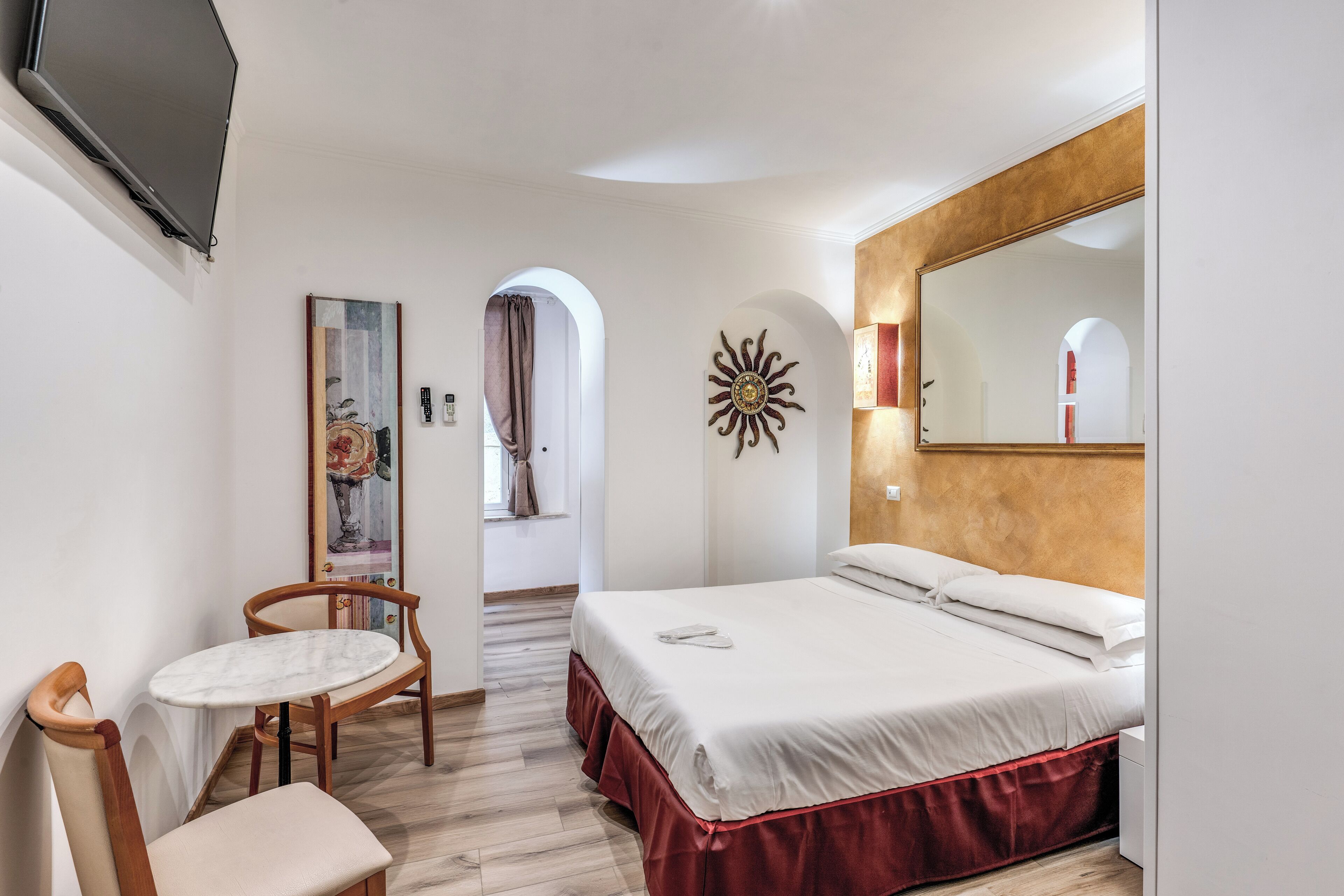 A hotel room with a bed, a chair, a table, and a large mirror.