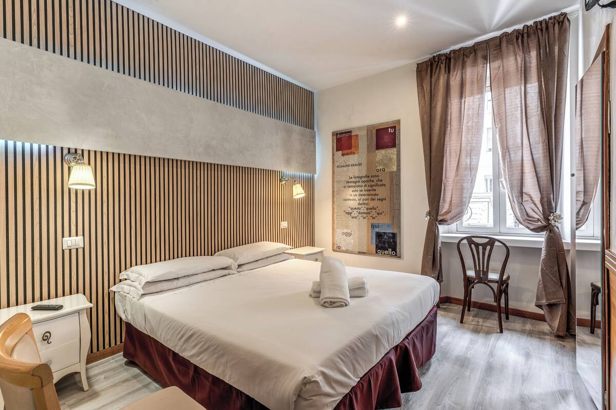A neatly arranged bedroom with a bed, bedside table, chair, and a poster on the wall.