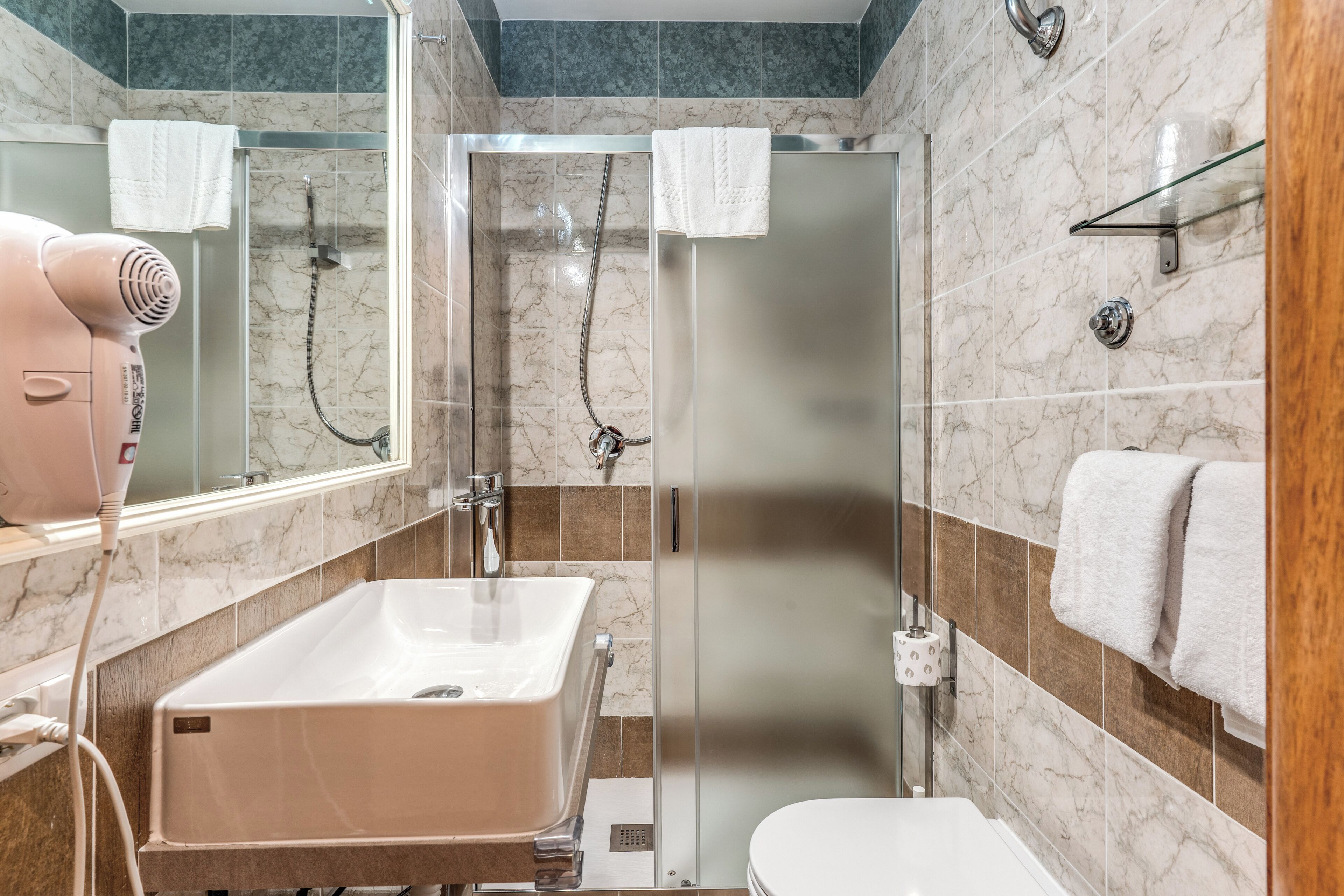 A bathroom with a marble-tiled wall, a glass shower enclosure, a white sink, and a hairdryer.