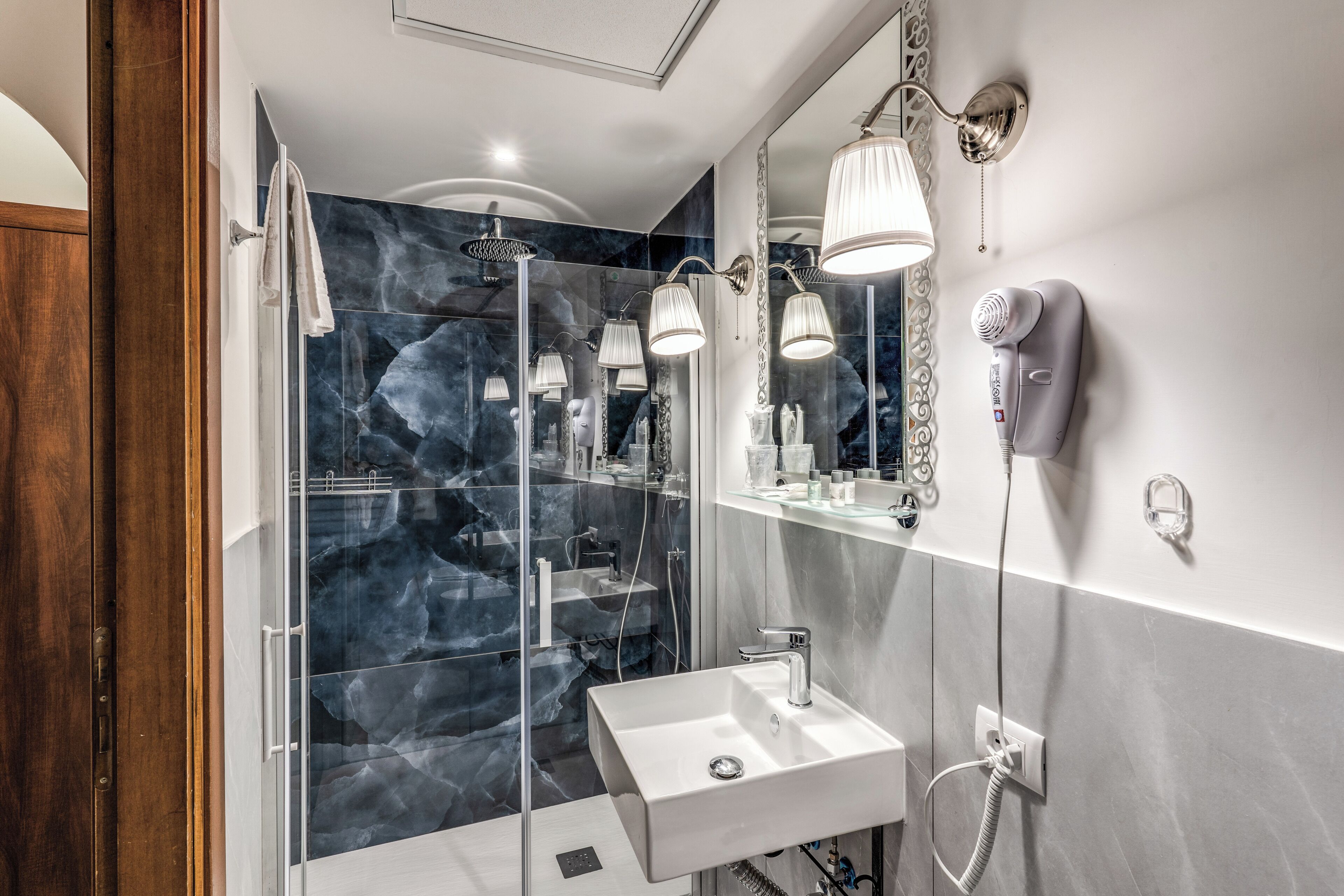 Ein modernes Badezimmer mit einer in Glas abgeschirmten Dusche, einem weißen Waschbecken und einem an der Wand befestigten Fön.