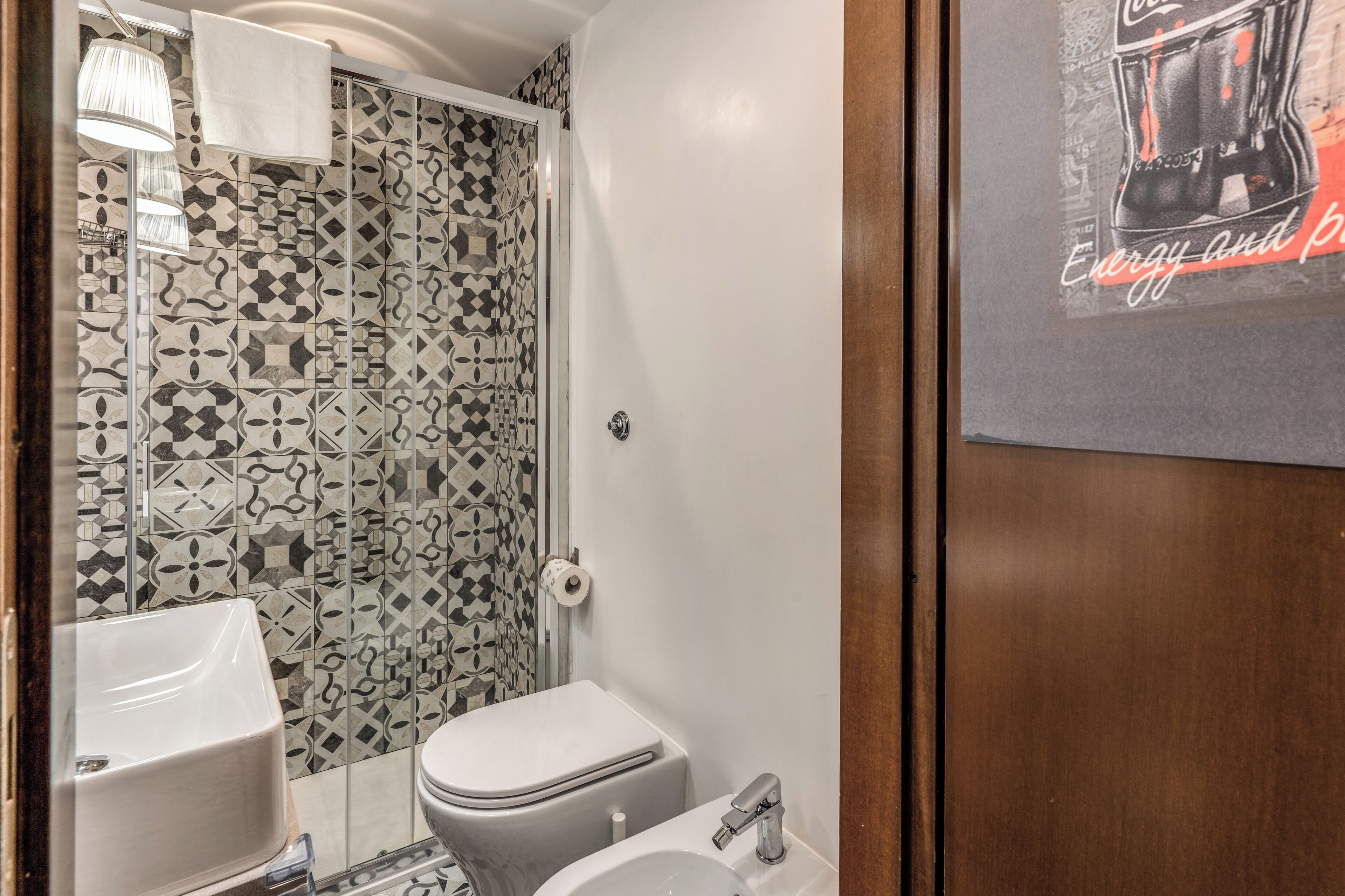 A bathroom with a patterned tile wall, a white sink, and a toilet.