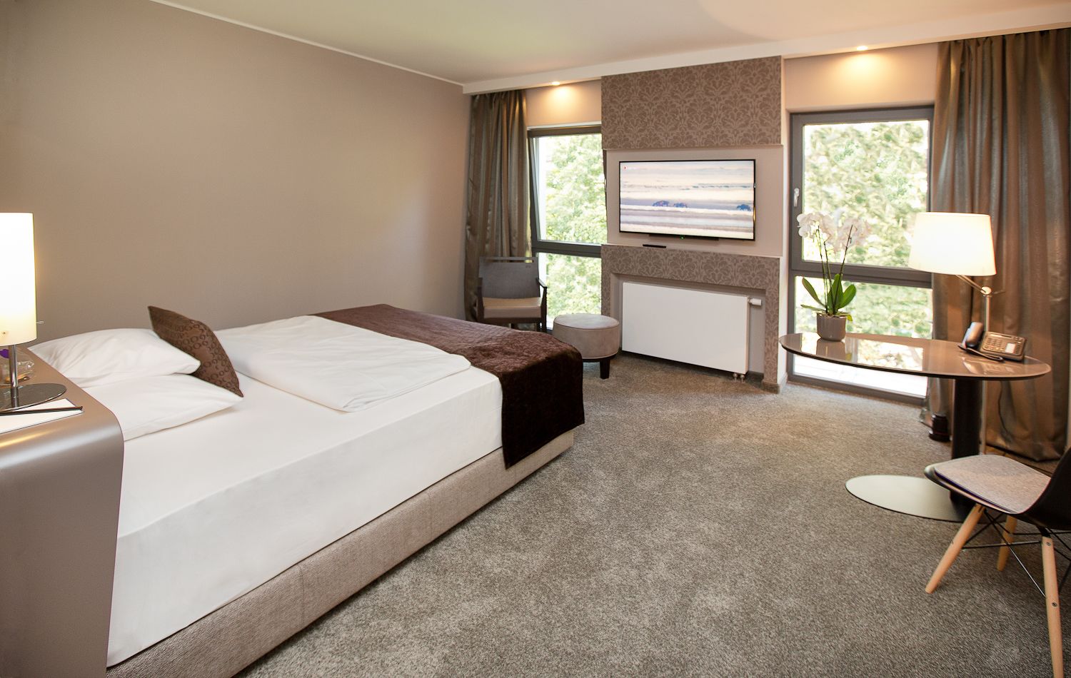 Ein Hotelzimmer mit einem großen Bett, einem Schreibtisch, einem Sessel, einem Fernseher und einem Vorhangfenster.
