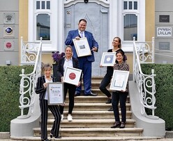 Un grupo de personas sosteniendo diplomas enmarcados en una escalera frente a un edificio con un letrero que dice 'Park Villa'.
