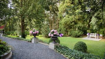 A garden pathway leading to a bench surrounded by lush greenery and flowering planters.