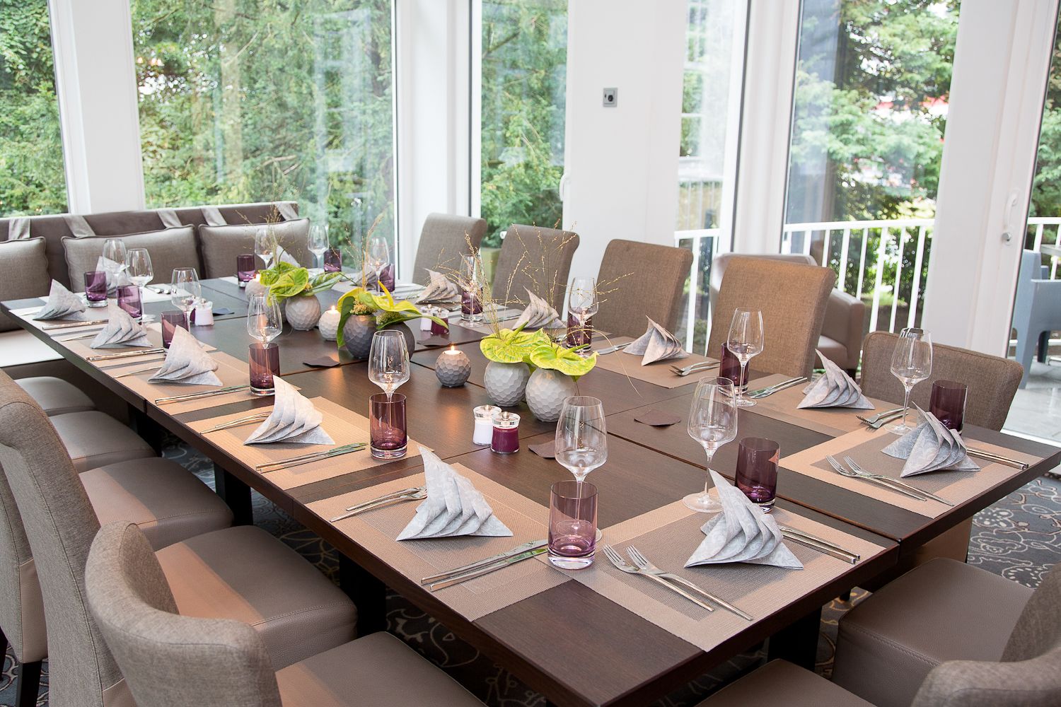 Une longue table à manger, dressée pour un repas, avec de nombreuses chaises, des bougies et des plantes décoratives.