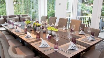 Une longue table à manger, dressée pour un repas, avec de nombreuses chaises, des bougies et des plantes décoratives.