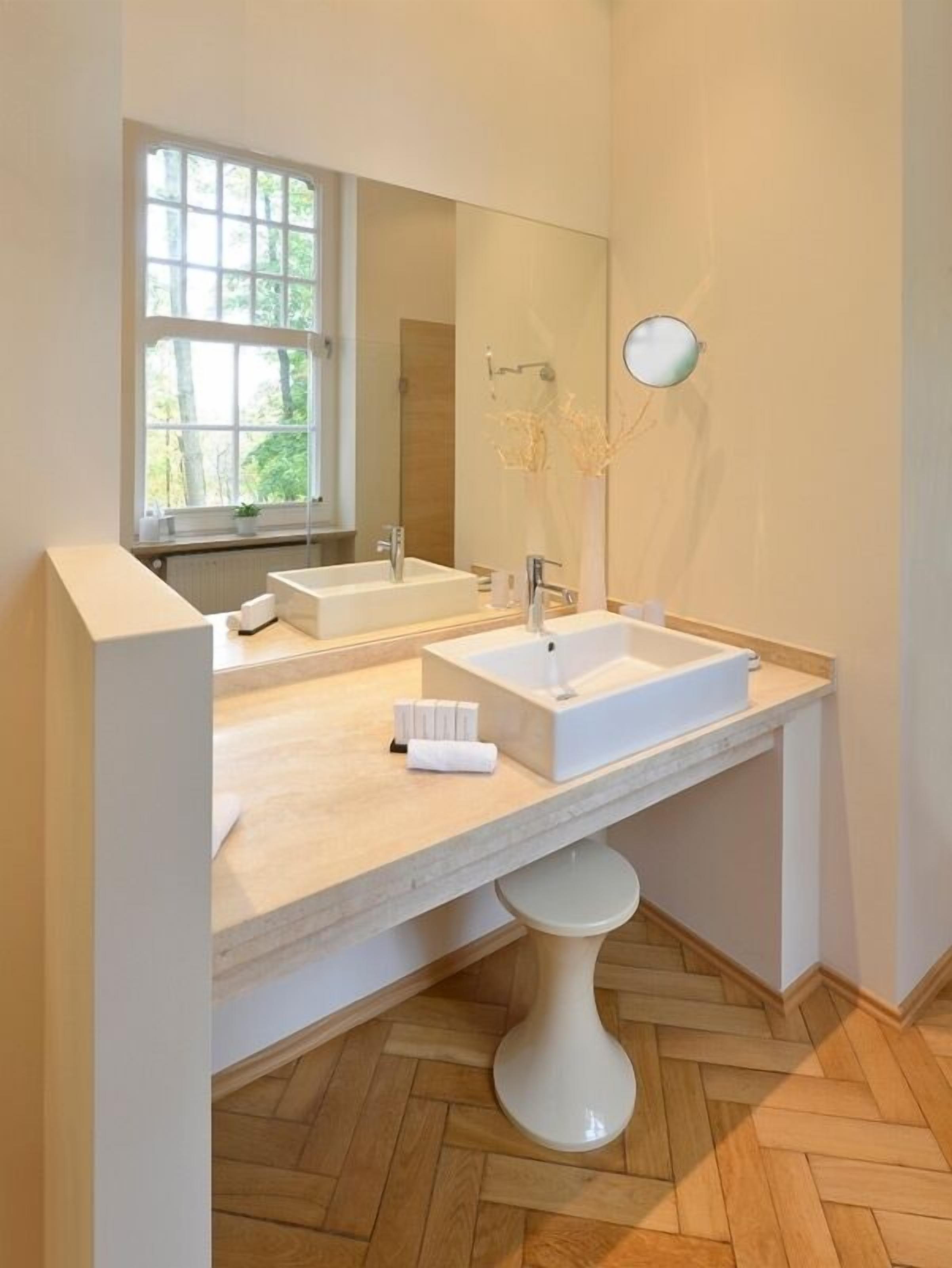 Un baño moderno con dos lavamanos, un espejo grande y un ventanal con vistas a árboles.