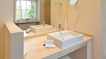 Un baño moderno con dos lavamanos, un espejo grande y un ventanal con vistas a árboles.