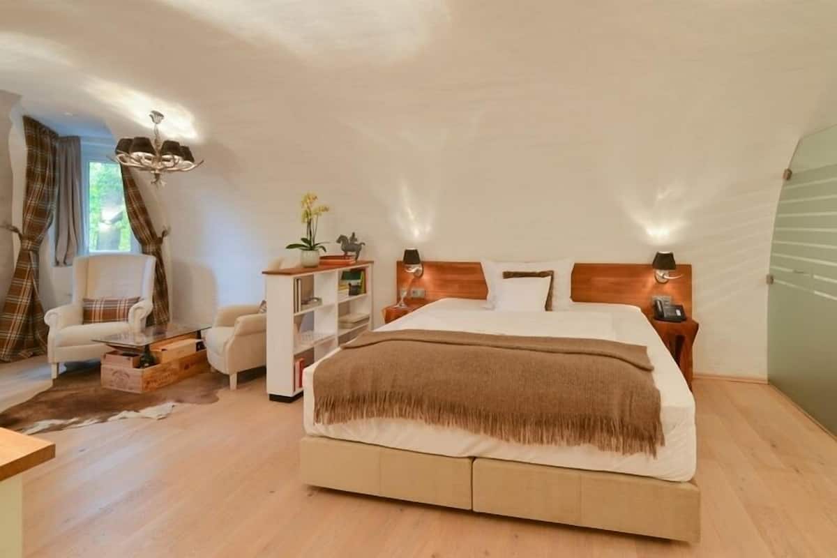 A bedroom with a large bed, a wooden nightstand, a white wardrobe, a chair, and a chandelier.