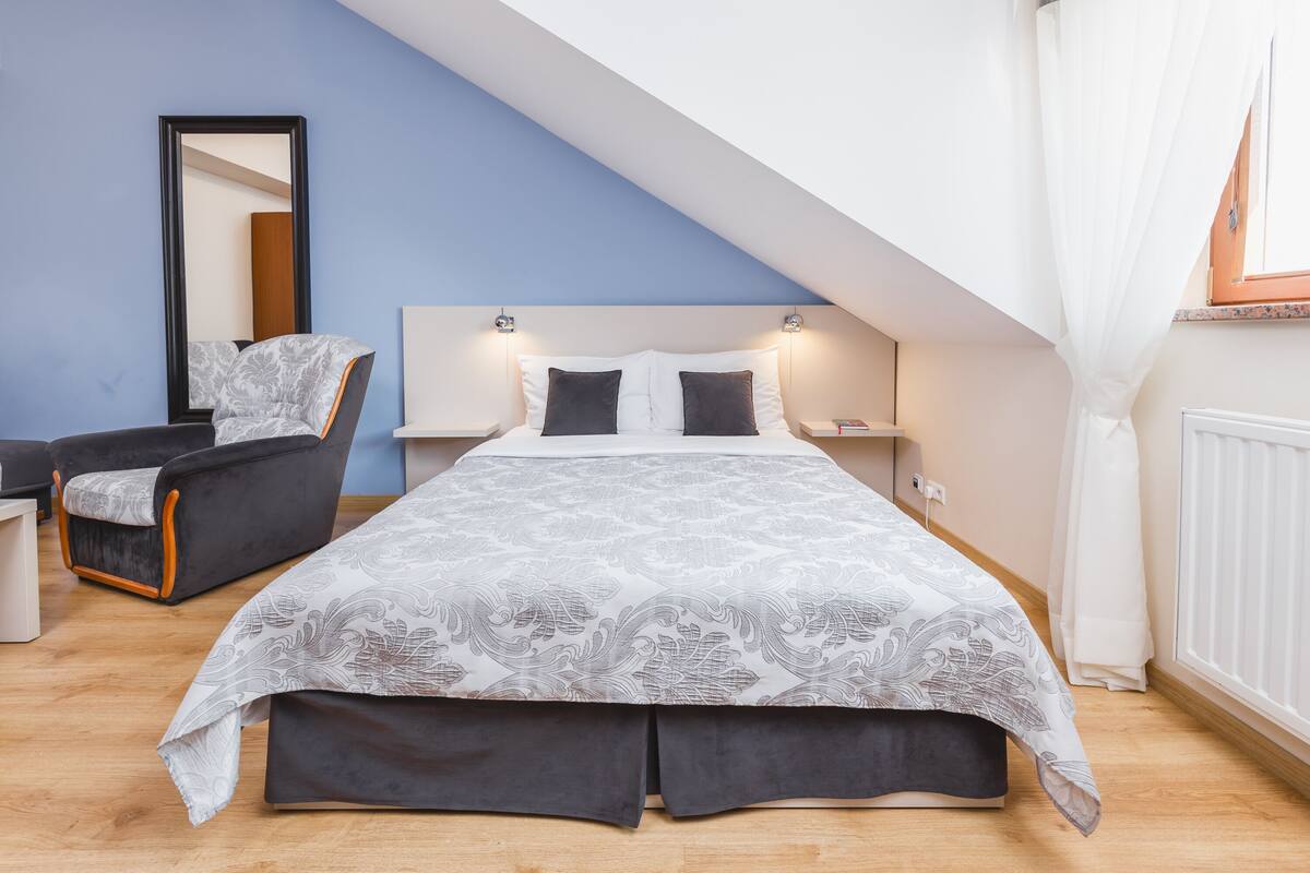 Un dormitorio con cama, una silla, una mesita de noche, un espejo y una ventana.
