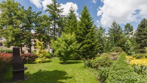 Un jardin bien entretenu, agrémenté de divers arbres et arbustes, d’un barbecue et d’un sentier.