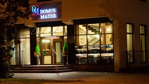 L’entrée d’un hôtel, avec une enseigne indiquant « DOMUS MATER » et un escalier menant à l’entrée.