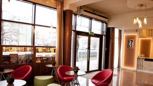 Un hall d'entrée moderne avec des fauteuils rouges et verts, un comptoir d'accueil et une bibliothèque contenant des ouvrages de voyage.