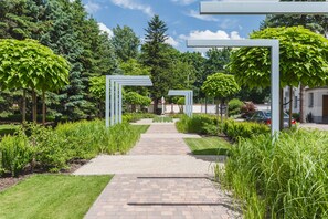 Un chemin pavé traverse un jardin où l’on trouve différentes espèces de plantes et d’arbres.