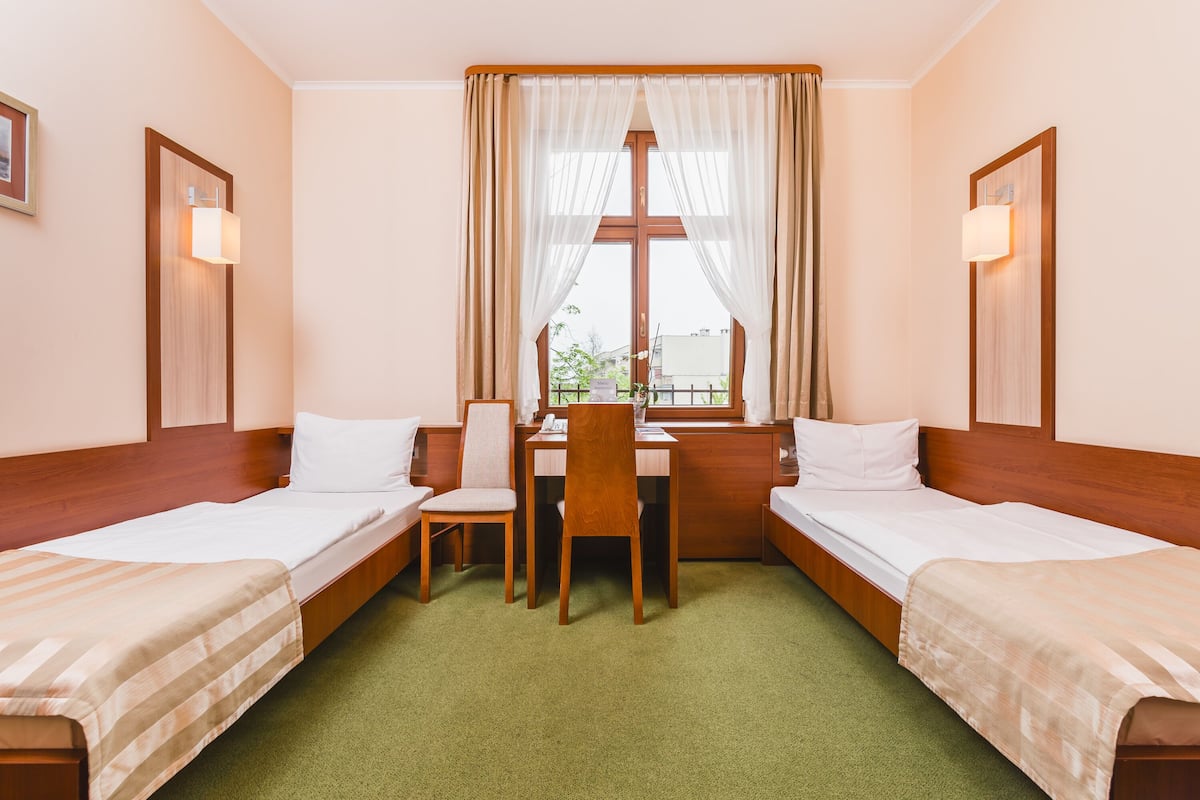 Habitación de hotel con dos camas individuales, un escritorio y una silla.