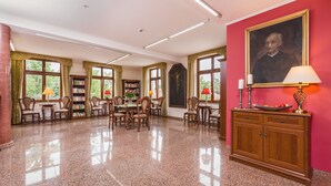 Une bibliothèque spacieuse avec des étagères, un coin repas et un mur rouge orné d’un portrait.
