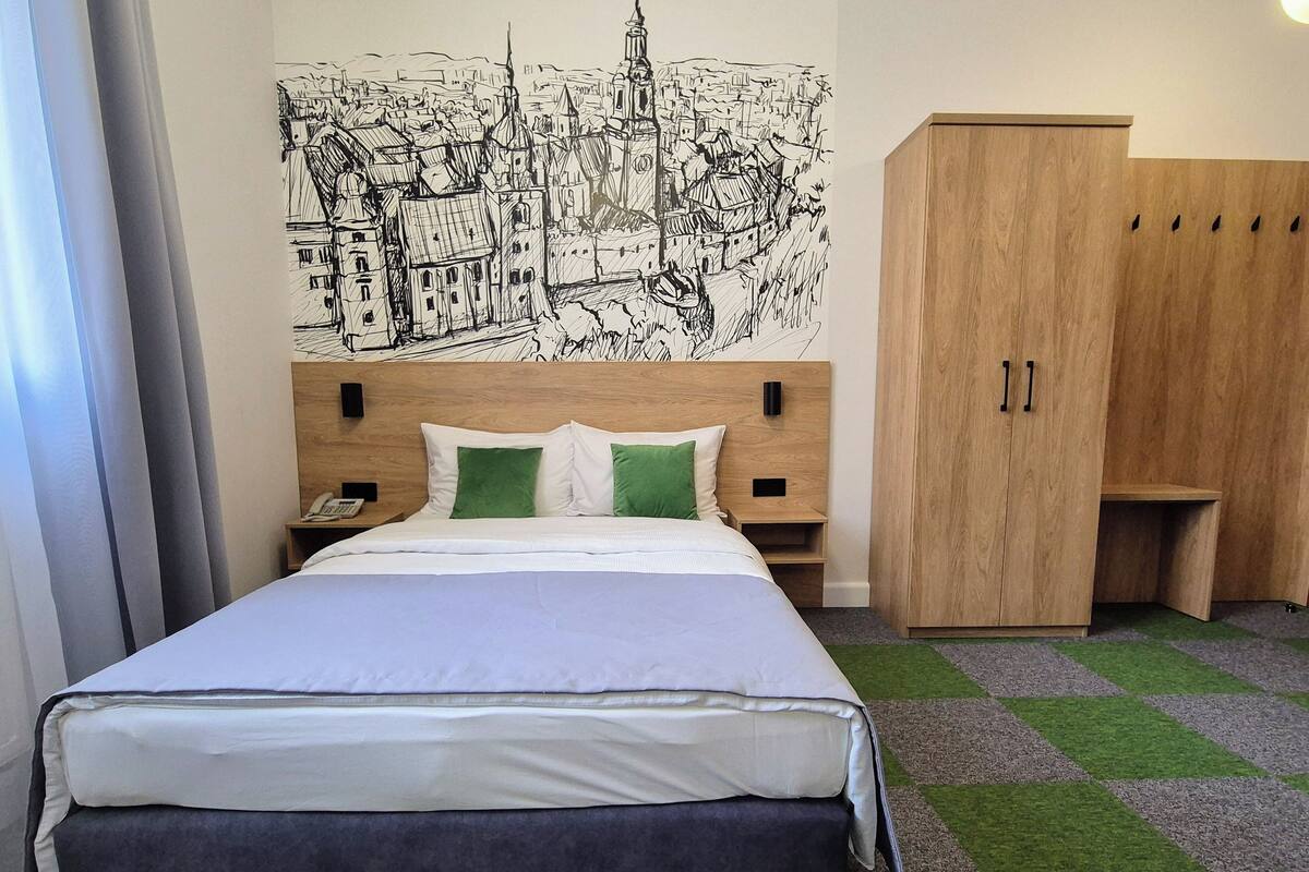 Una habitación de hotel con cama, armario de madera, mesita de noche y un mural en la pared.