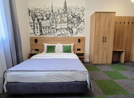A hotel room with a bed, a wooden wardrobe, a nightstand, and a wall mural.
