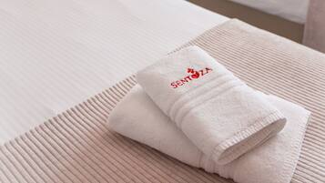 A hotel room with two beds, each with a neatly folded towel and a bedside lamp.
