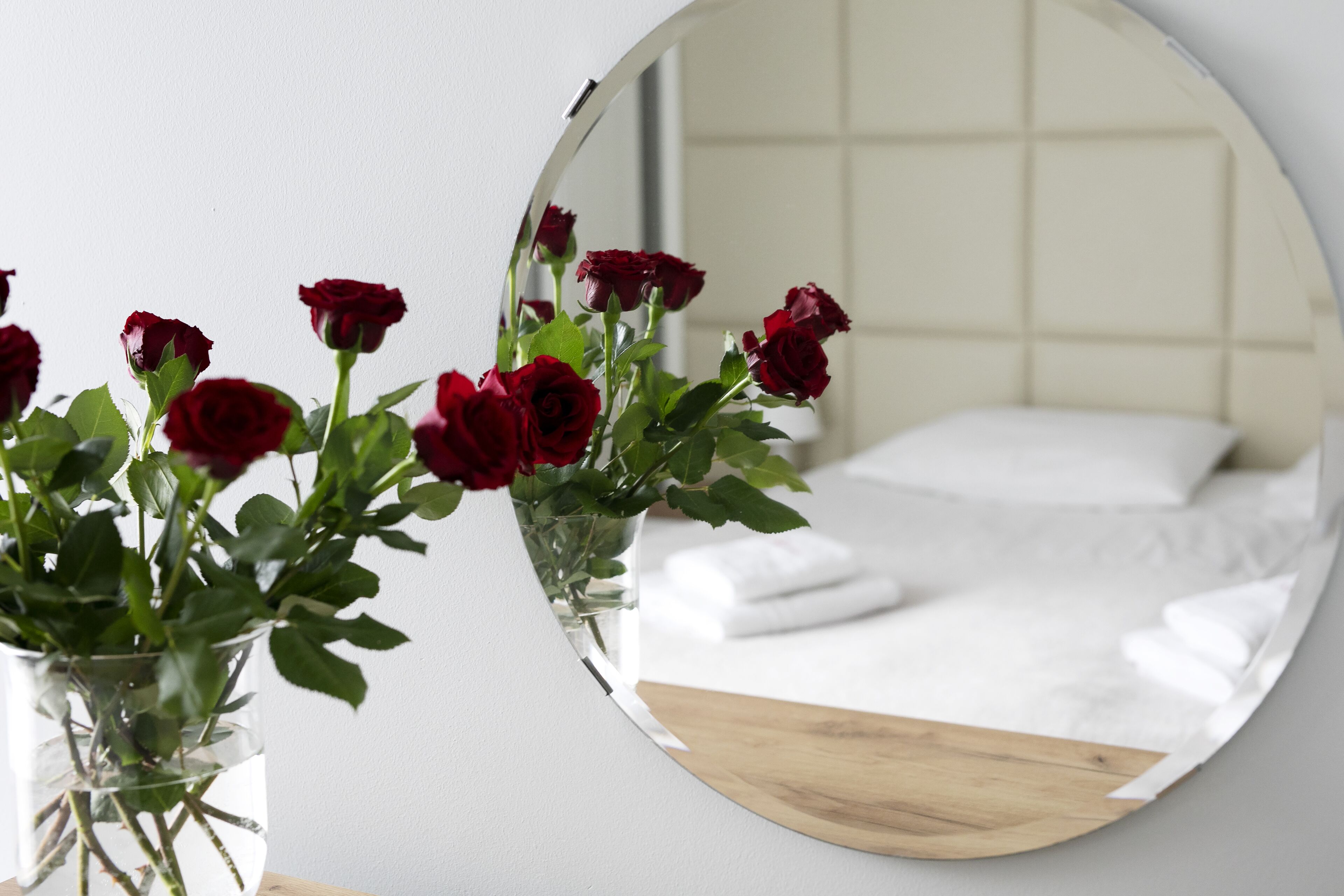 A mirror reflecting a bed with white linens and a wooden headboard.