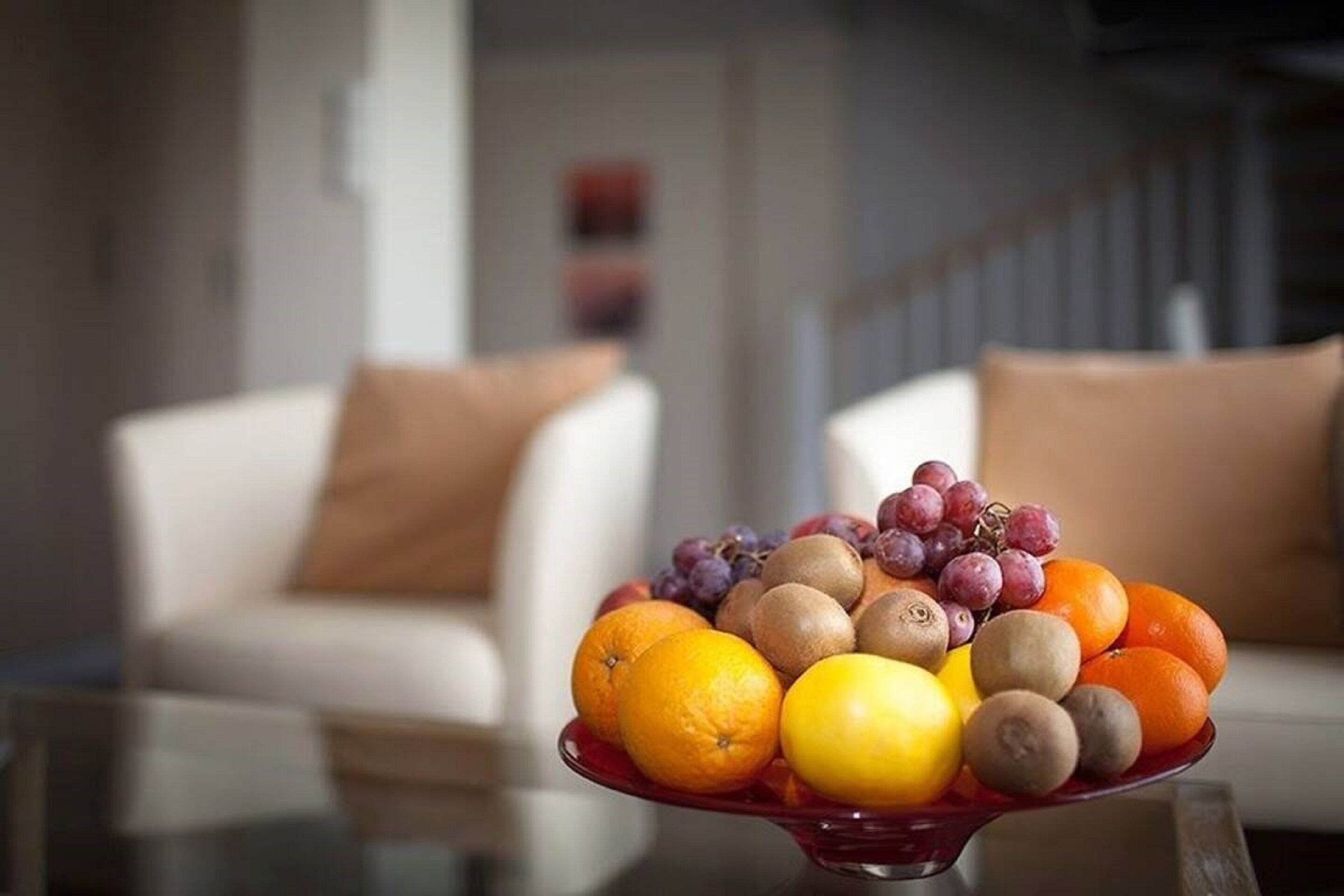 Un frutero sobre una mesa en una sala de estar, con un sofá blanco y una escalera al fondo.