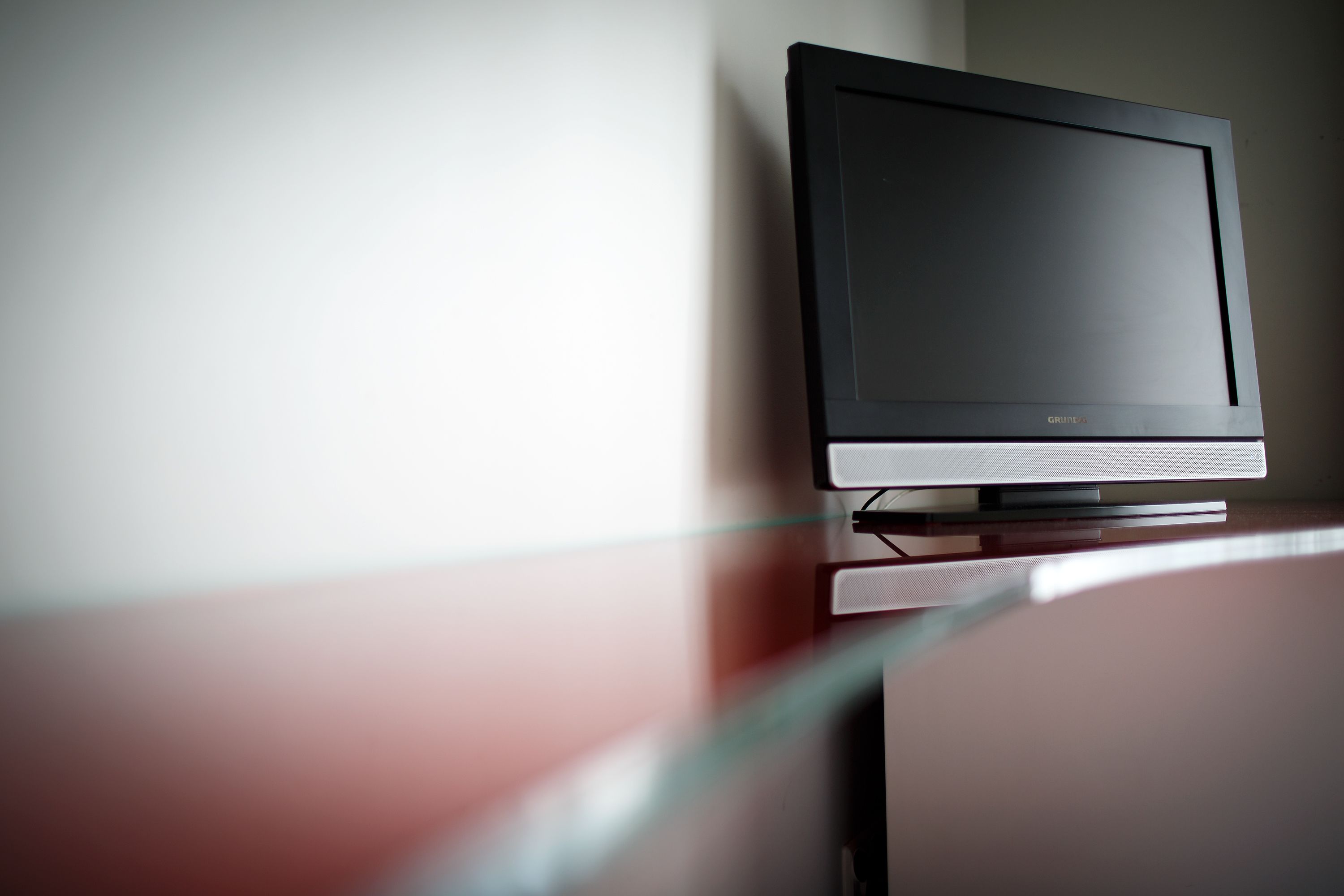 A television on a stand in a room with a plain wall and a curved wooden surface.