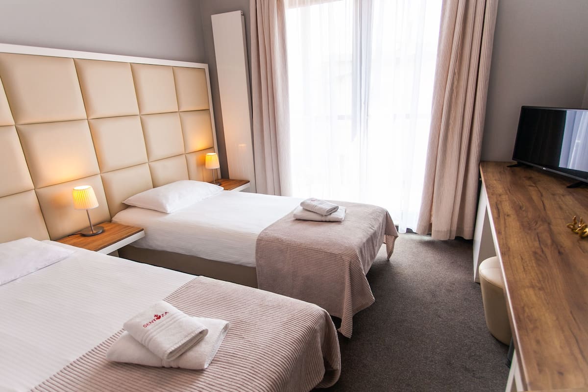 A hotel room with two beds, a wooden desk, a television, and a window with curtains.