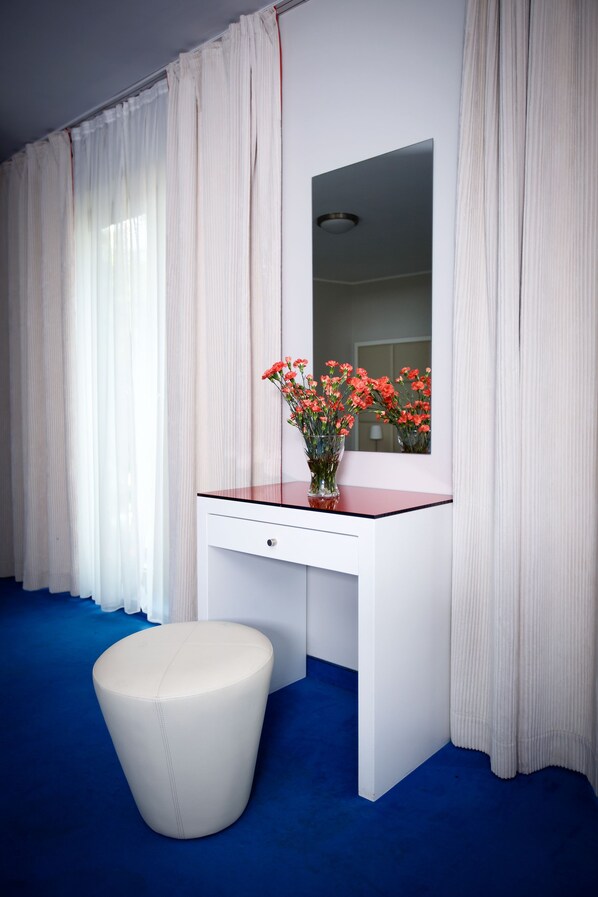 A room with a white desk, a mirror, and a vase with flowers.