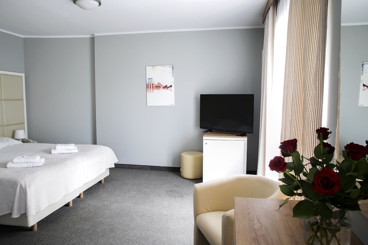 A hotel room with a bed, a TV, a small table with a vase of flowers, and a chair.