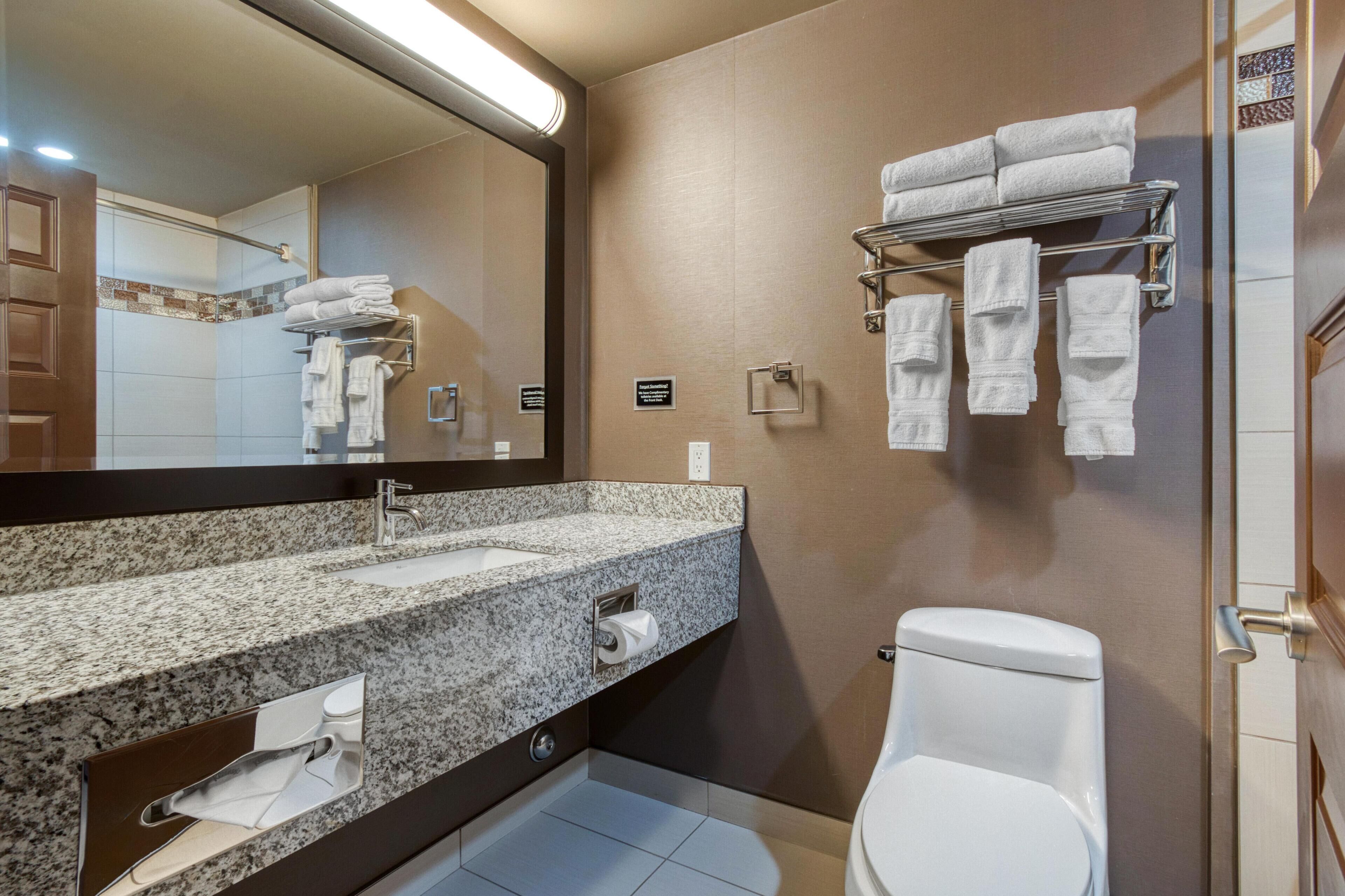 A modern bathroom with a granite countertop sink, a mirror, a towel rack, and a toilet.