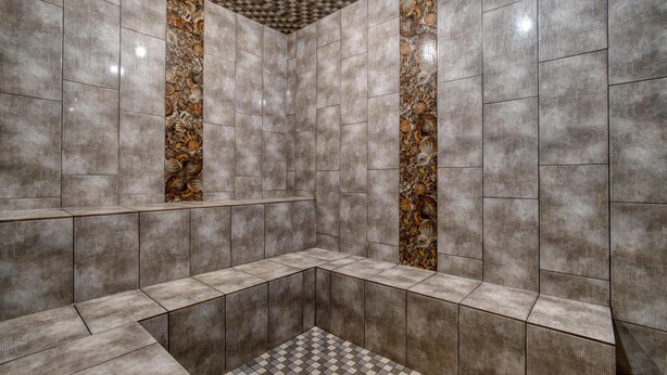 A modern bathroom with grey tiles, a checkered floor, and a central column with a decorative pattern. - Best Western Plus Fox Creek (Fox Creek)