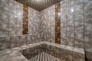 Ein modernes Badezimmer mit grauen Fliesen, einem Schachbrettfußboden und einer zentralen Säule mit dekorativem Muster.
