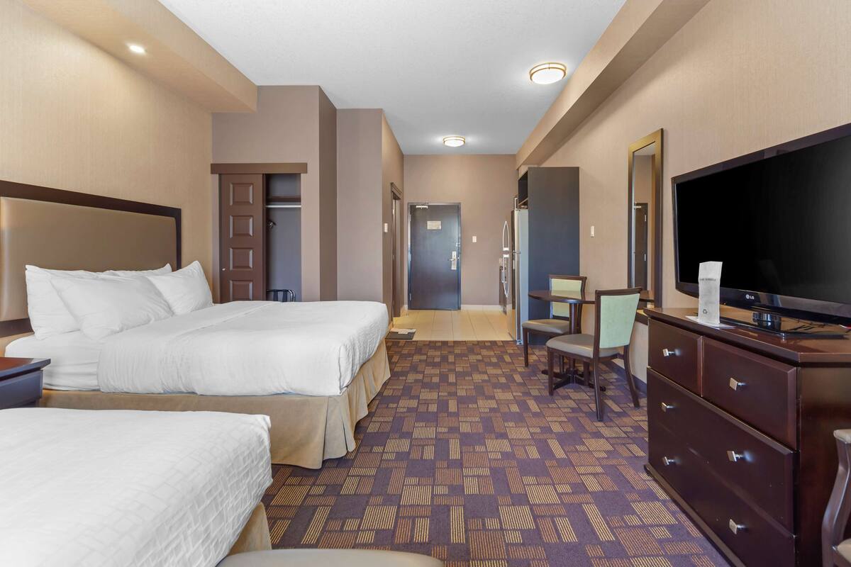 A hotel room with two beds, a television, a dresser, and a mirror.