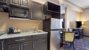 A compact kitchen with a microwave, refrigerator, and a dining area with a chair and table. - Best Western Plus Fox Creek (Fox Creek)