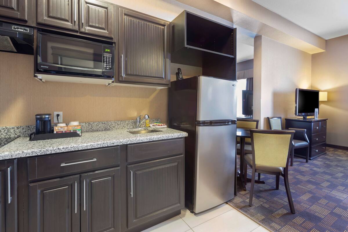 A compact kitchen with a microwave, refrigerator, and a dining area with a chair and table.
