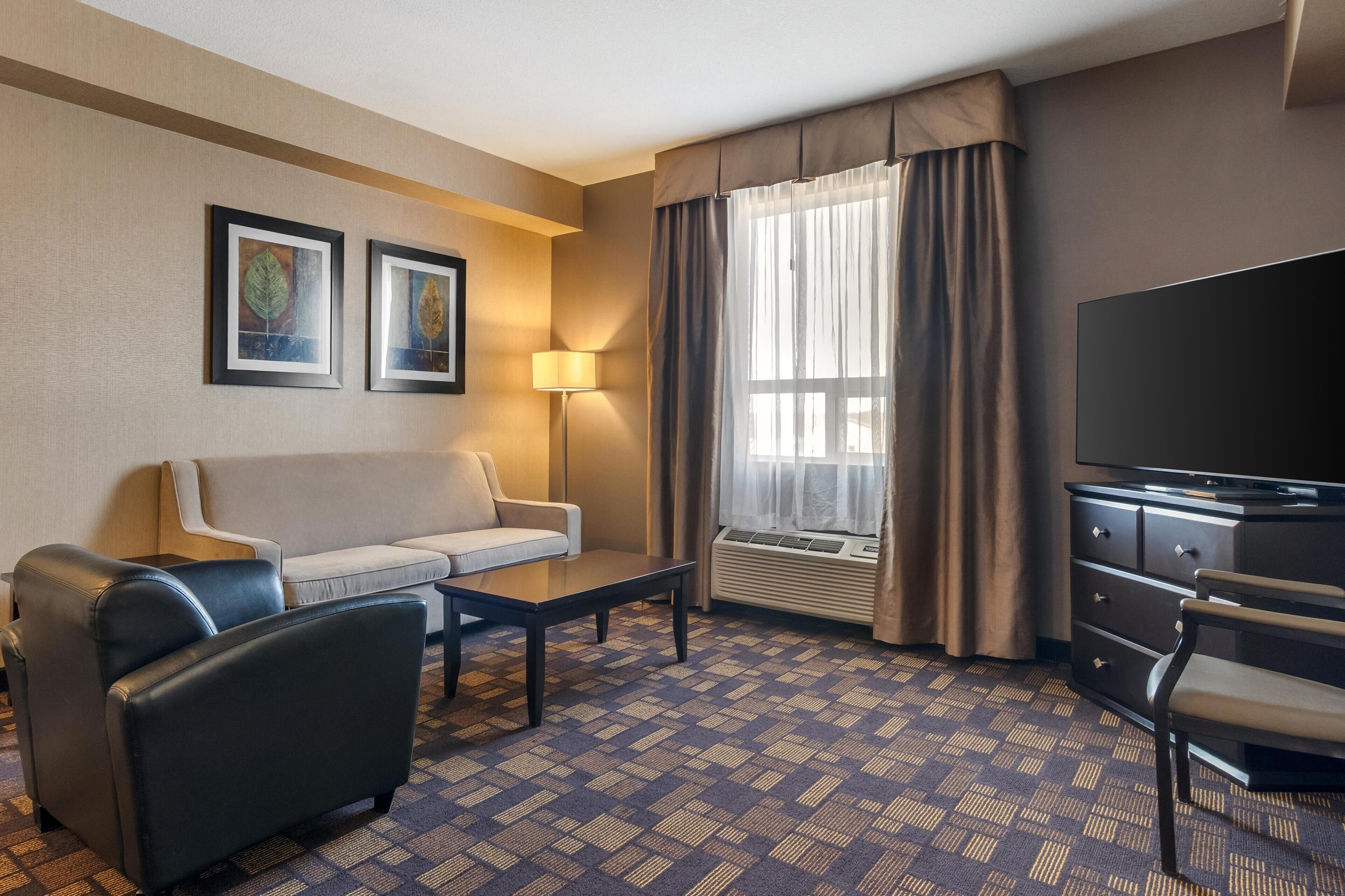 A hotel room with a sofa, armchair, TV, and a patterned carpet.