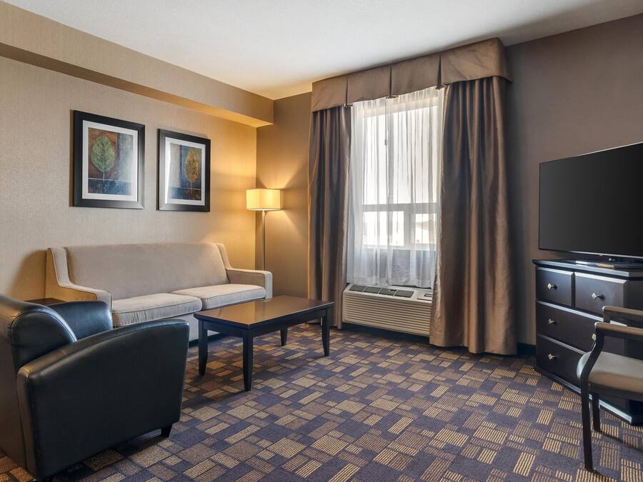 A hotel room with a sofa, armchair, TV, and a patterned carpet.