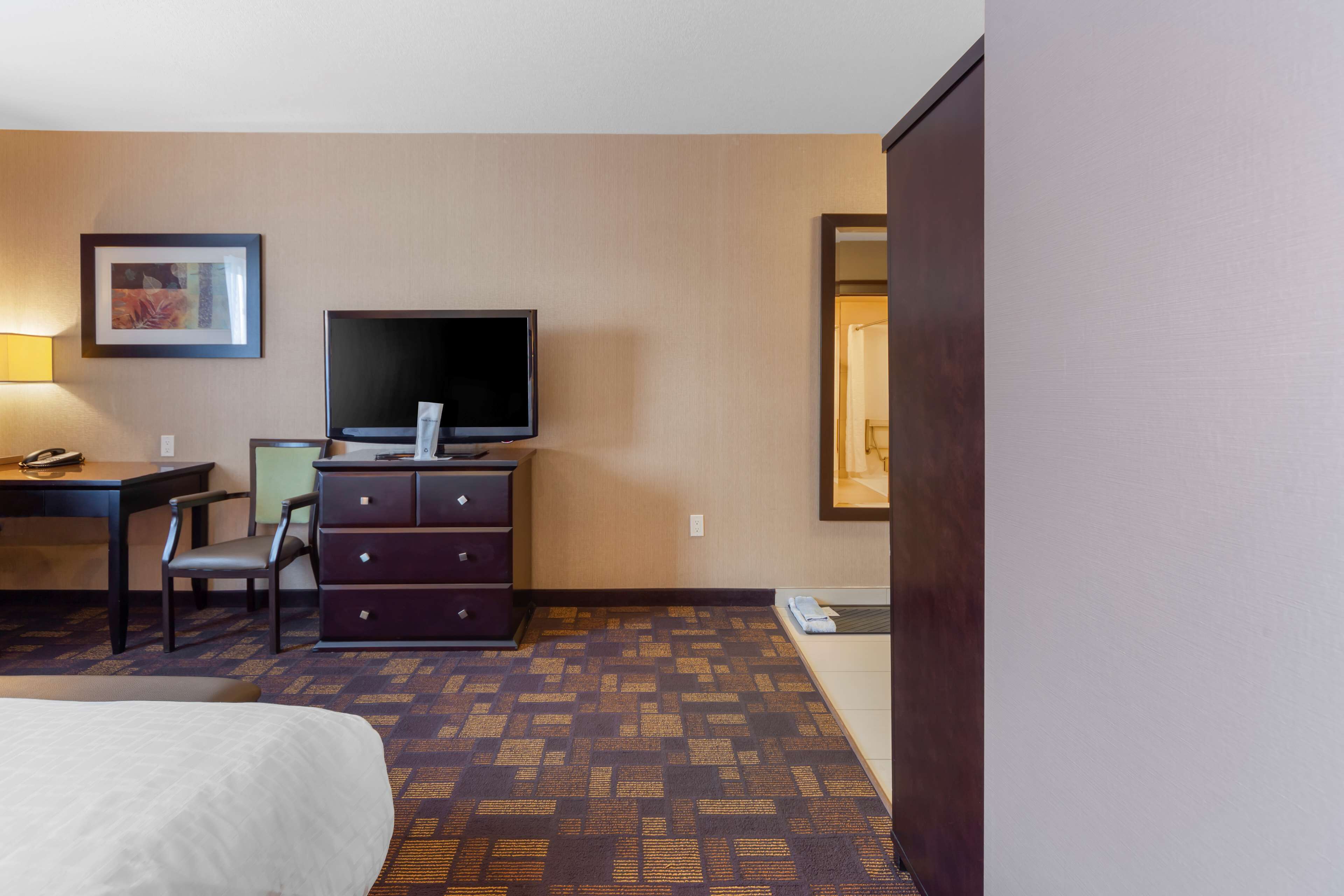 A hotel room with a bed, a desk with a chair, a dresser, a television, and a framed picture on the wall.