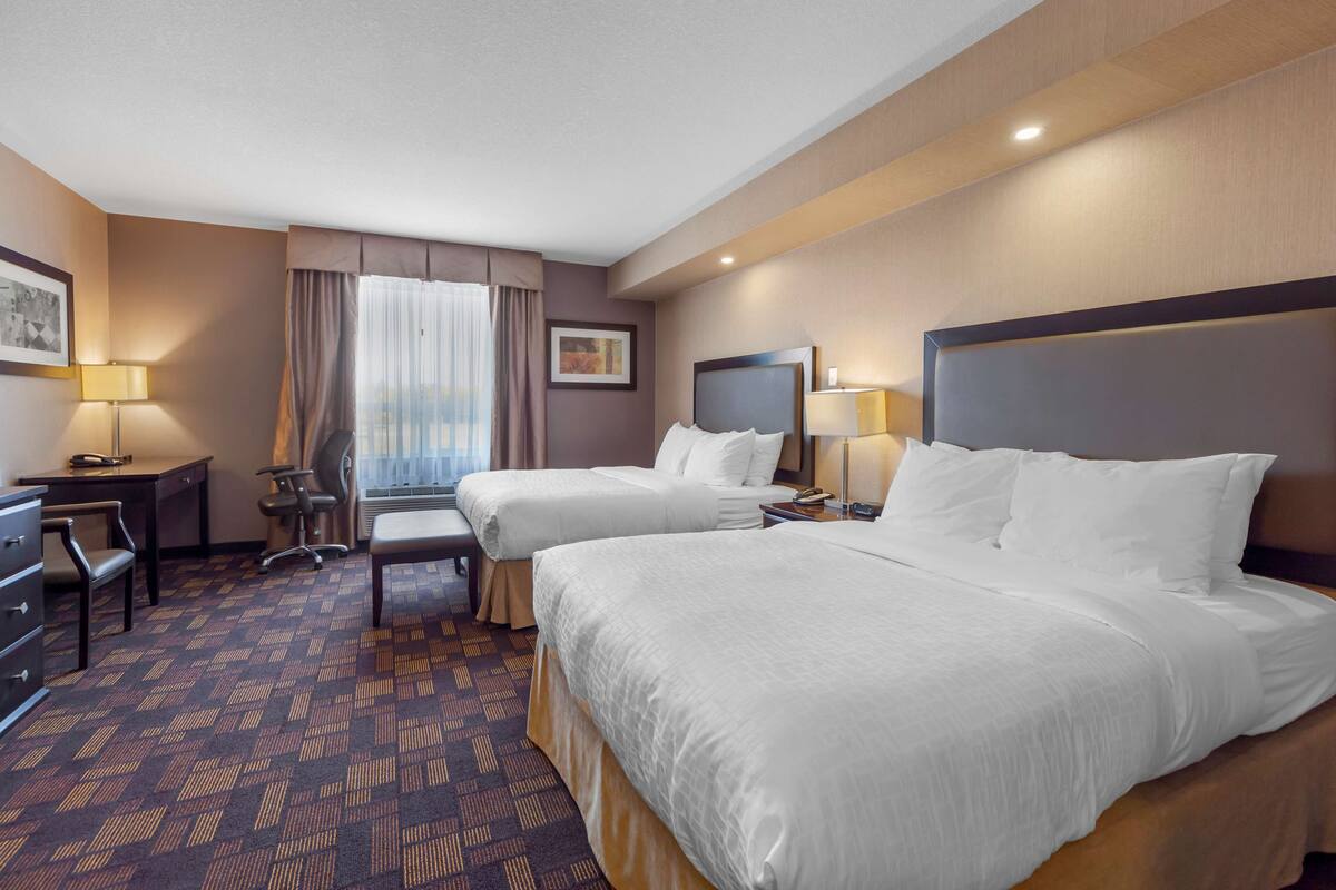 A hotel room with two beds, a desk, a chair, and a window with curtains.