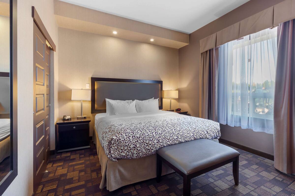 A hotel room with a large bed, bedside tables, a bench, and a view of the city through the window.