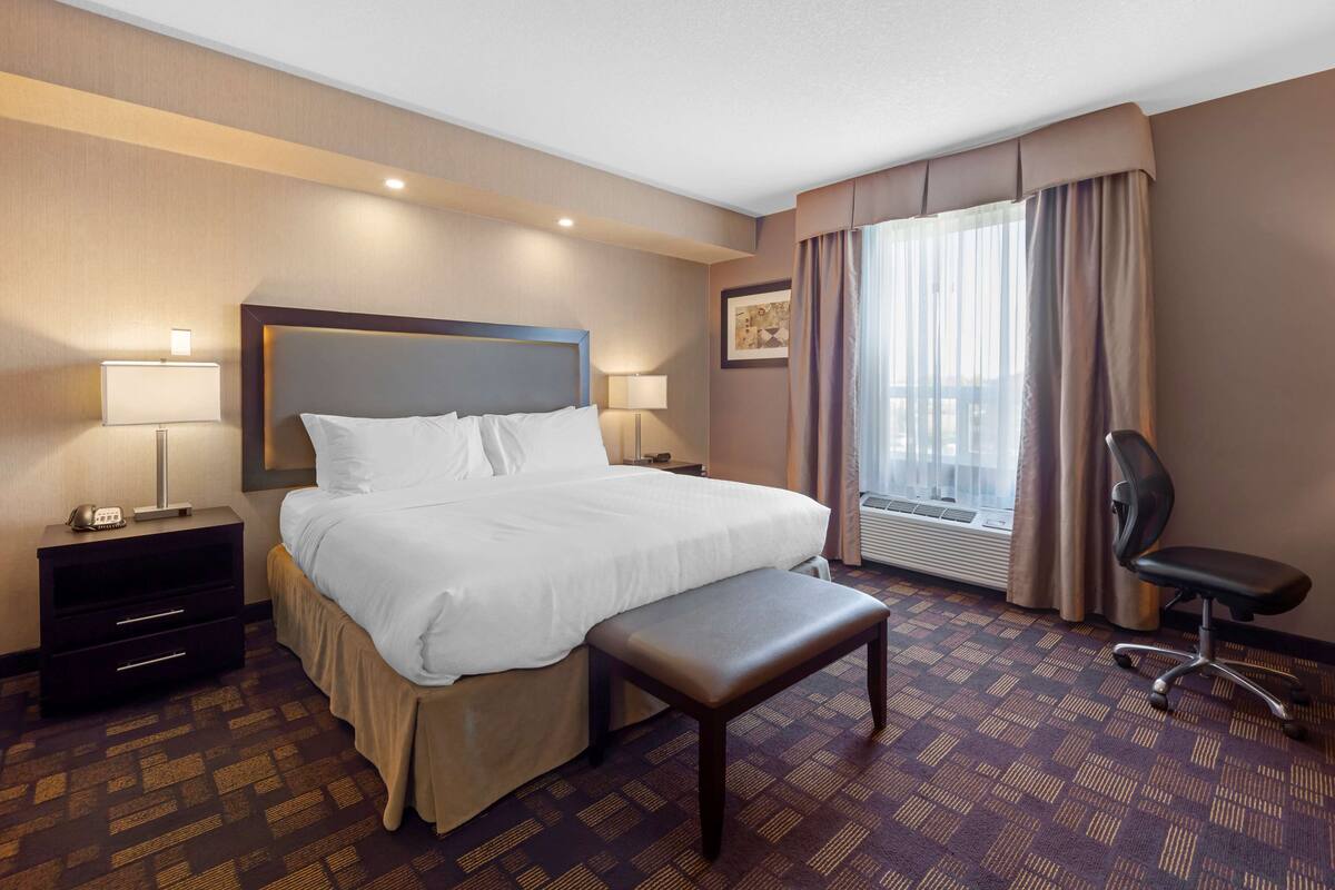 A hotel room with a large bed, bedside tables, a desk, a chair, and a window with curtains.