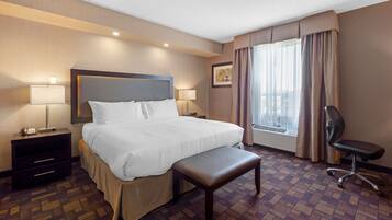 A hotel room with a large bed, bedside tables, a desk, a chair, and a window with curtains.