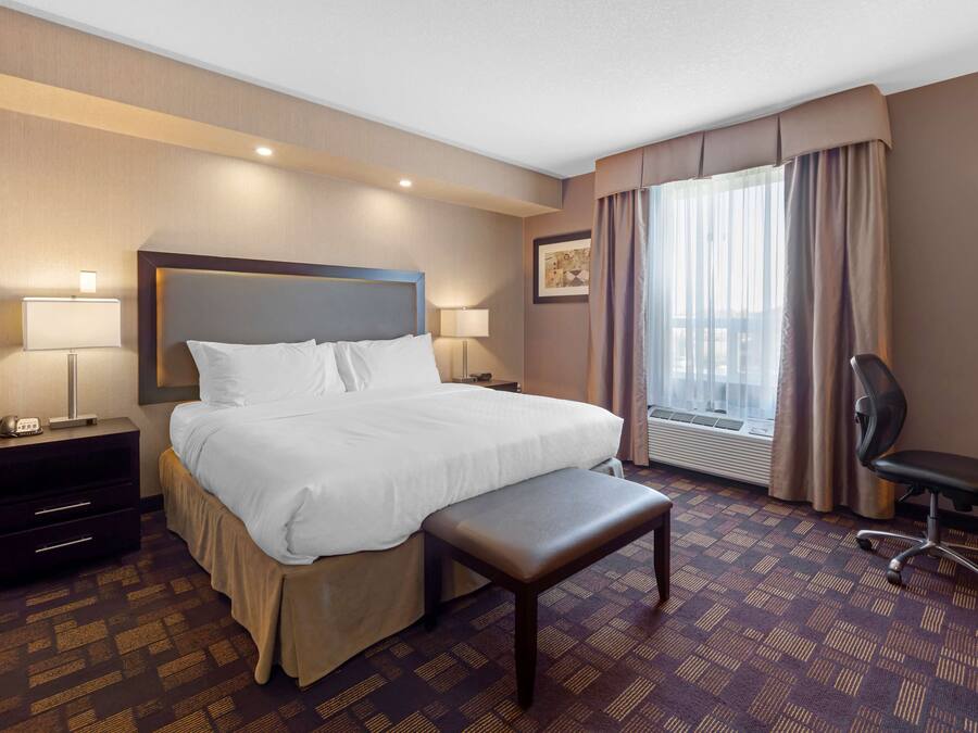 A hotel room with a large bed, bedside tables, a desk, a chair, and a window with curtains.